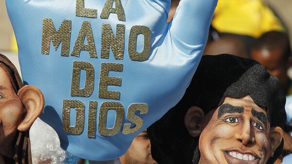 Аргентинский болельщик в маске, изображающей Марадону, и с перчаткой, на которой написано: Рука бога перед матчем Аргентина - Нигерия группового этапа ЧМ 2010 - Sputnik Mundo