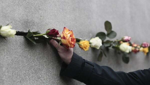 Un hombre coloca una flor en una grieta del Muro de Berlín - Sputnik Mundo