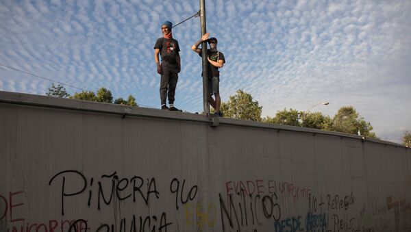 Manifestantes chilenos contra el Gobierno de Chile parados sobre un muro en Santiago - Sputnik Mundo