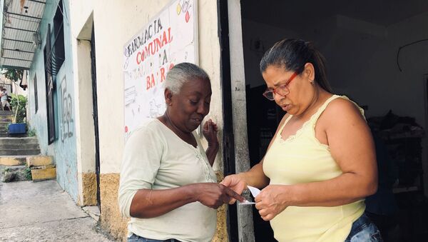 Manuela, dueña de la casa donde está la farmacia comunal, entregando unos medicamentos a una vecina del barrio - Sputnik Mundo