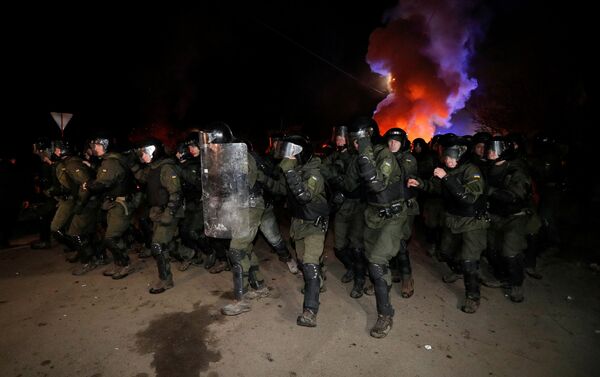 Policías ucranianos despejan el camino de los manifestantes que lo bloquean durante una protesta contra la llegada de un avión que transporta a los evacuados de China - Sputnik Mundo