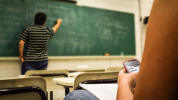 Una estudiante con el móvil da clase en un aula  - Sputnik Mundo